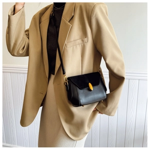Close-up of black crossbody bag with gold oval lock and textured leather detail