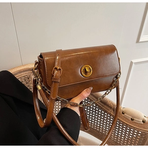 Detail of a brown vintage leather handbag featuring a gold round lock and metal chain strap