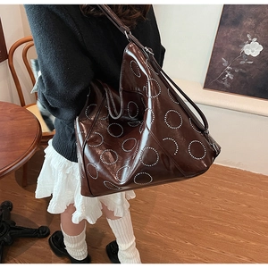 Detail of coffee brown tote bag with silver rivet circles on shiny synthetic leather