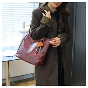 Dettaglio borsa tote in pelle bordeaux con ciondolo a orsetto e logo in rilievo