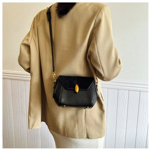 Detail of the black leather crossbody bag featuring a golden oval buckle and studs