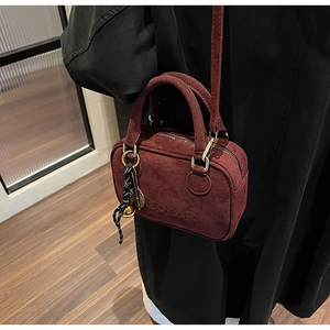 Detalle del bolso de ante burdeos con logotipo EDEAR grabado y adorno dorado colgante