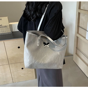 Detail of silver metallic tote bag with unique butterfly pendant and crinkled texture