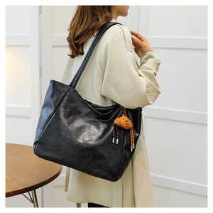 Dettaglio della borsa tote in pelle nera con logo impresso e ciondolo a forma di orso