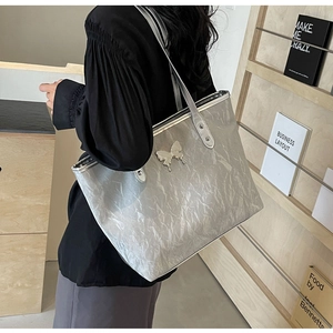 Detail of silver metallic tote bag with pleated texture and stylish butterfly ornament