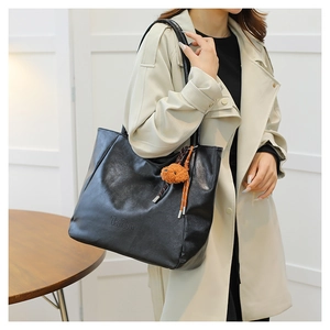 Dettaglio della borsa tote in pelle nera con logo goffrato e ciondolo a forma di orsetto