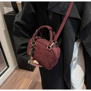 Detalle de bolso de ante rojo vino con logotipo EDEAR grabado y correa de cuero