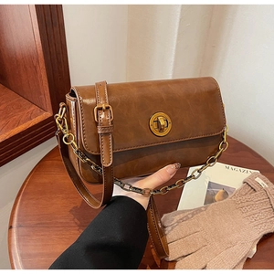 Close-up of brown vintage crossbody bag featuring a golden circular twist lock and chain strap