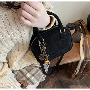 Detalle del bolso de ante negro con colgante de raqueta dorada y logo en relieve