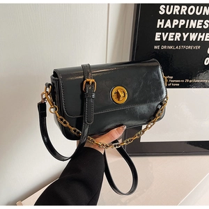 Macro detail of glossy black leather handbag featuring golden twist lock and chain strap
