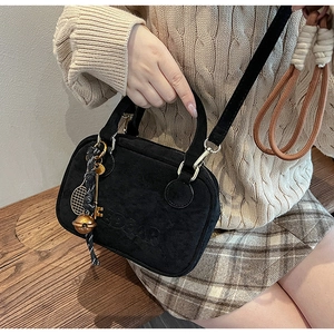 Detalle de bolso negro con textura de ante, letras grabadas y colgante decorativo