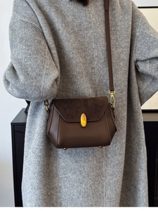 Brown leather crossbody bag with gold hardware shown on a grey textured winter coat
