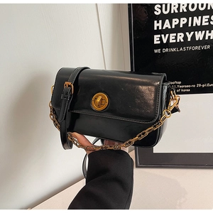 Detailed close-up of a glossy black square bag with a vintage gold twist lock and chain strap