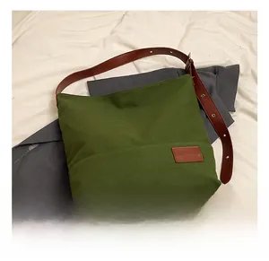 Detail of green canvas tote bag featuring brown leather strap and metal buckle adjustment