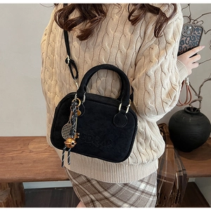Detalle del bolso de ante negro con grabado DEAR y colgante de raqueta de tenis dorado