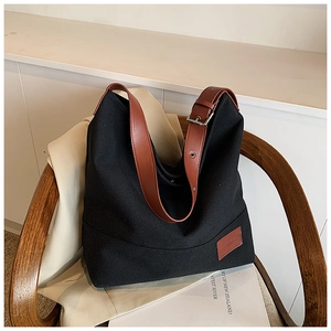 Detail of black canvas tote bag with brown leather strap on a wooden chair