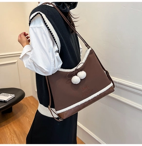 Detailed view of brown tote bag with fuzzy faux shearling trim and white pompom charm
