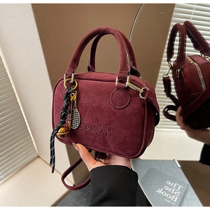 Detalle de bolso burdeos mate con herrajes dorados y un colgante de raqueta de tenis