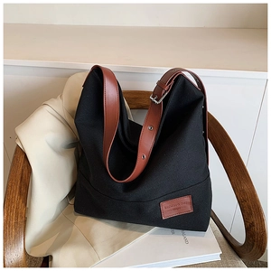Detail of black canvas tote bag with brown leather straps and silver buckle on wooden chair