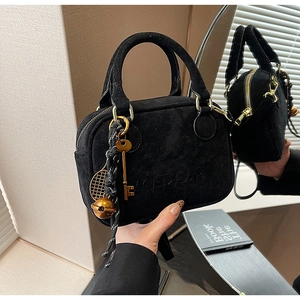 Detalle del bolso de ante negro con colgantes de tenis dorados y logo Mepfar