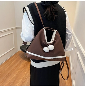 Detail of a brown PU leather shoulder bag with white faux fur trim and fluffy pompoms