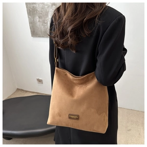 Close-up of brown suede tote bag with leather logo patch worn by model in black blazer