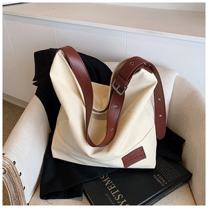 Close-up of beige canvas tote bag with brown leather strap and metal buckle detail