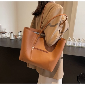 Close-up of caramel brown tote bag with zipper pocket shown on a model in a cafe