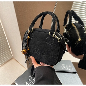 Detalle del bolso de ante negro con relieve FEDEAR y colgantes decorativos de metal oro