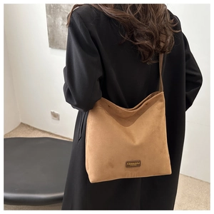 Detail of brown suede bucket bag with leather patch showing logo on black trench coat