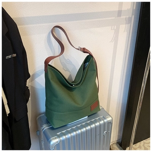 Detail of dark green canvas hobo bag with adjustable brown leather strap on suitcase