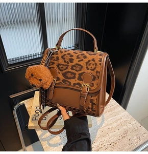Detail view of leopard print plush bag with brown faux leather trim and teddy charm
