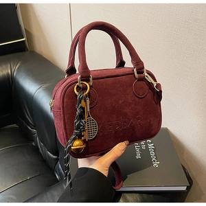 Detalle de bolso de ante burdeos con letras en relieve y adorno de raqueta de tenis