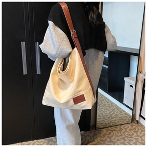 Detail view of large canvas tote bag with adjustable brown leather strap and logo patch