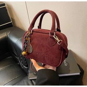 Detalle de bolso burdeos de ante sintético con logotipo EDEAR y colgante de tenis
