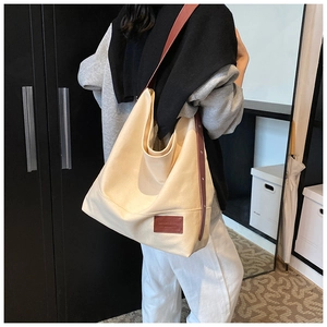 Detail of beige canvas tote bag with brown leather strap worn by a female model
