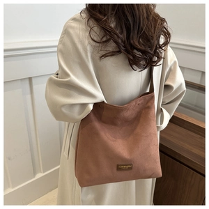 Detailed view of terracota suede tote bag with leather logo tag on beige coat