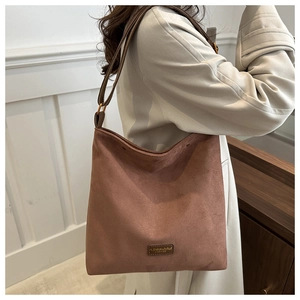 Detailed side view of brown suede tote bag with adjustable strap and metal logo plate