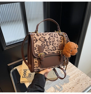 Detail of leopard print backpack with brown leather accents and a plush bear charm