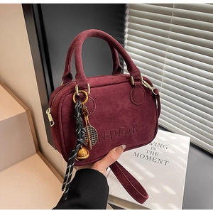 Detalle de bolso burdeos de ante sintético con cremallera dorada y colgantes trenzados