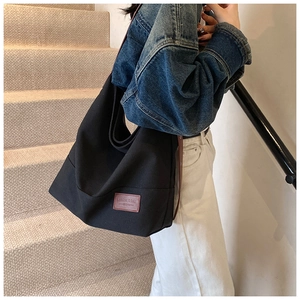 Detailed close-up of large black canvas tote bag featuring brown leather logo patch