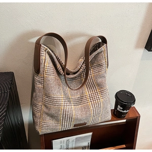 Detail of checkered fabric tote bag with brown leather handles on a wooden rack