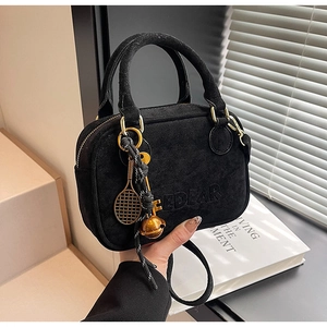 Detalle de bolso de ante negro con logo grabado y colgantes de raqueta de tenis bajo luz