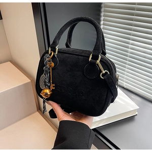 Detalle de bolso de ante negro con herrajes dorados, logo grabado y colgantes decorativos