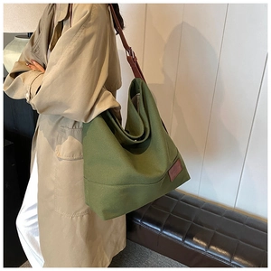 Detail of army green canvas tote bag with brown leather strap worn by a model