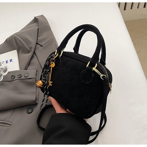 Detalle de bolso bandolera negro mate con herrajes dorados y colgante de llave de cuerda