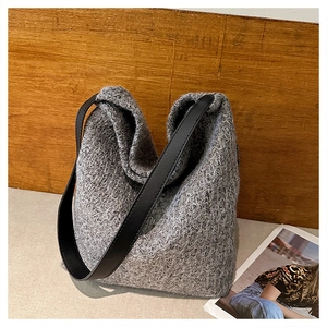 Dettaglio della borsa tote in tweed grigio con tracolla nera su sfondo in legno caldo