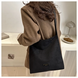 Detail of black suede tote bag styled with a brown blazer in a cozy indoor setting