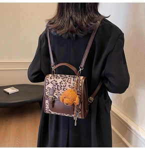 Detailed back view of leopard print backpack with brown leather straps and puppy charm