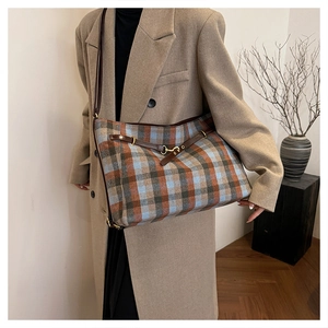 Détail du cabas à carreaux avec bandoulière en cuir et boucle dorée sur manteau camel